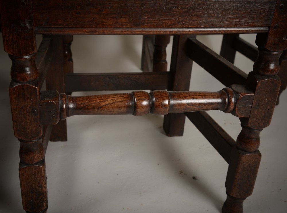 A set of four late seventeenth-century dark oak dining chairs featuring carved scroll top crestings, vertical back slats, solid panel seats, and turned stretchers. View IV