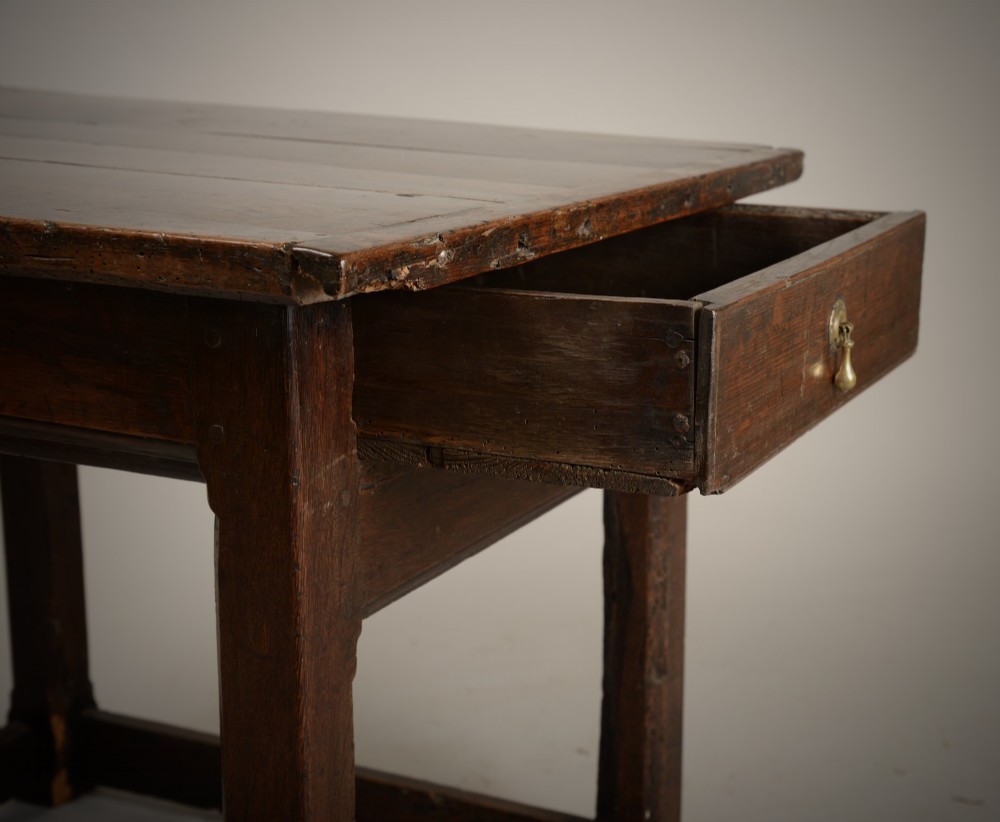 An antique dark oak low table featuring a plank top, a small side drawer with a brass drop handle, and sturdy legs joined by rectangular stretchers. View V
