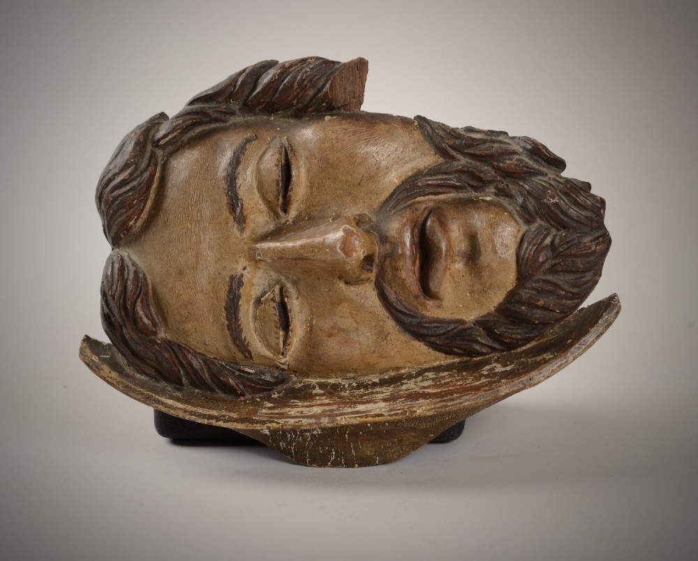 A carved wooden sculpture depicting the head of Saint John the Baptist resting on a circular charger platter.