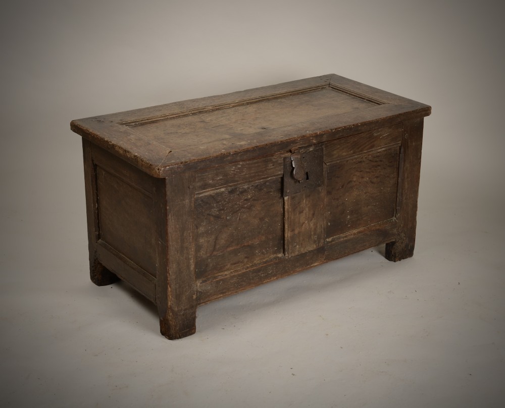 A dark 16th-century oak coffer featuring a hinged panelled lid, framed front panels, a central wrought-iron lock plate, and sturdy stile feet.