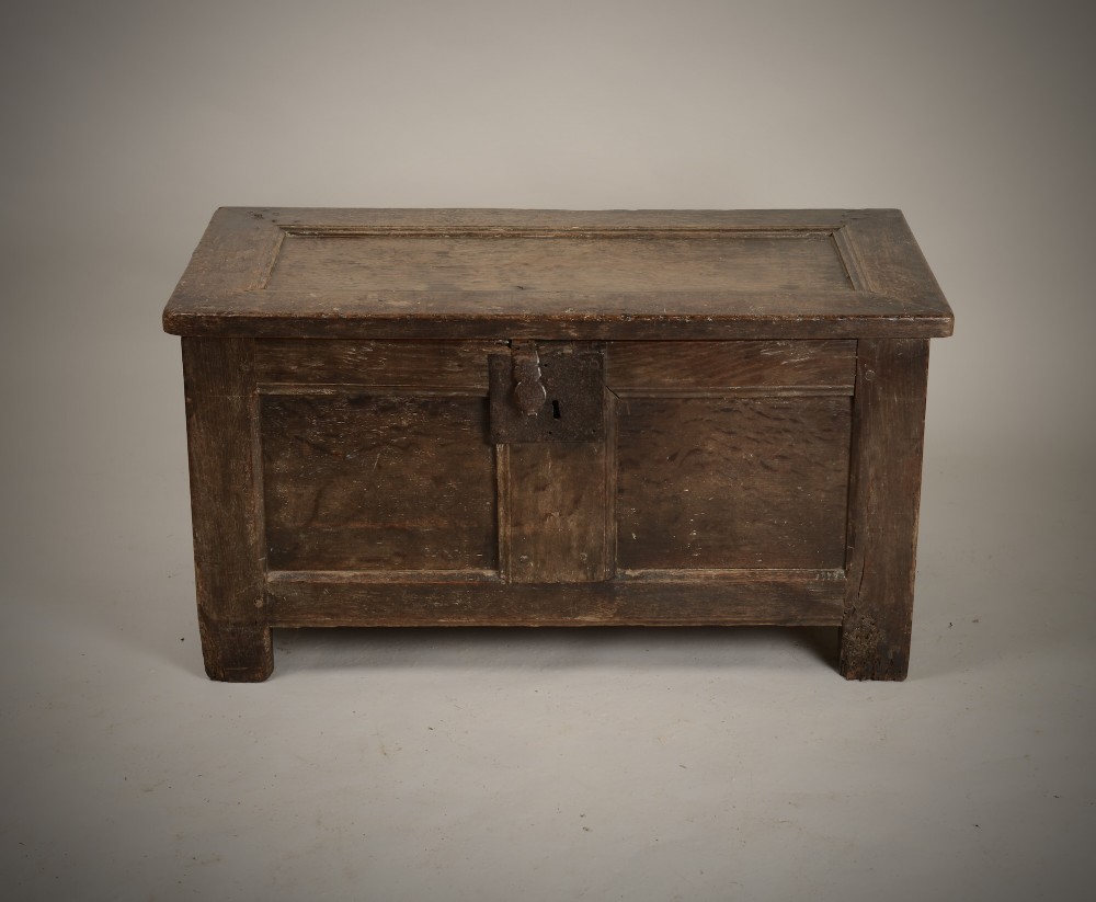 A dark 16th-century oak coffer featuring a hinged panelled lid, framed front panels, a central wrought-iron lock plate, and sturdy stile feet. View II