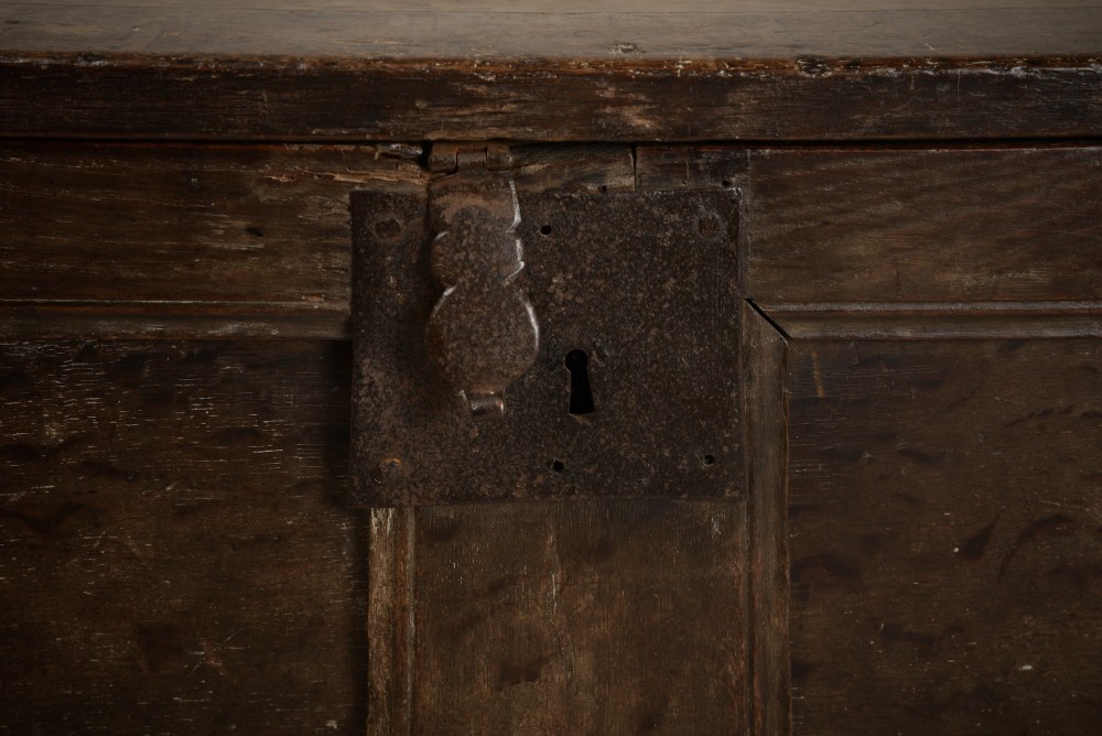 A dark 16th-century oak coffer featuring a hinged panelled lid, framed front panels, a central wrought-iron lock plate, and sturdy stile feet. View III