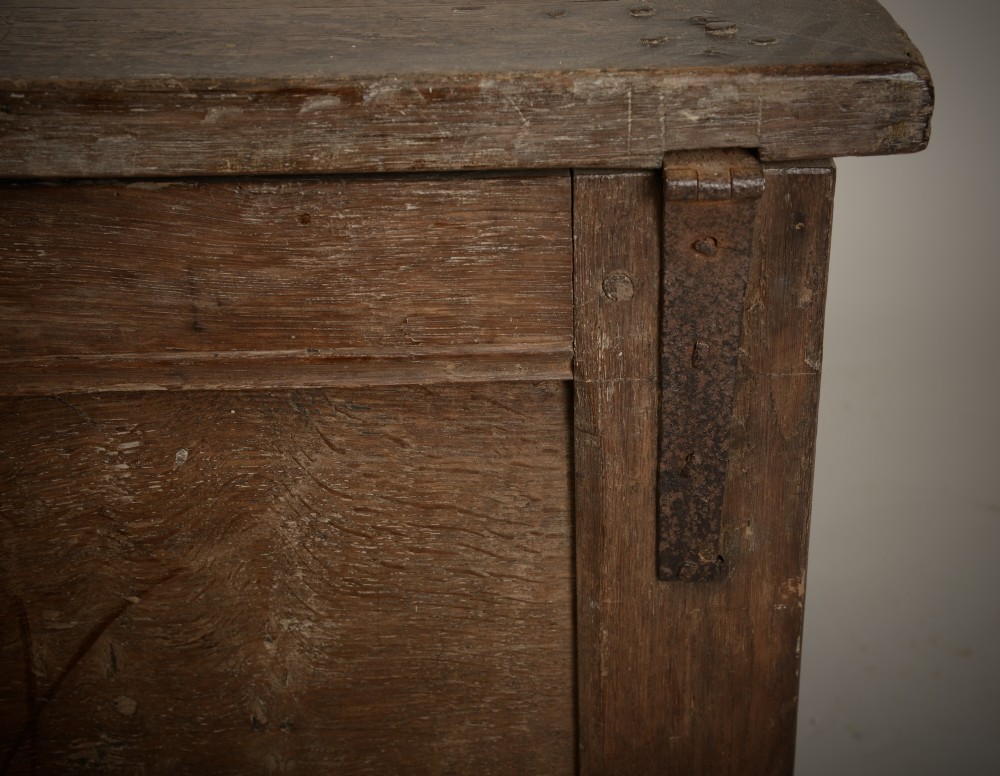 A dark 16th-century oak coffer featuring a hinged panelled lid, framed front panels, a central wrought-iron lock plate, and sturdy stile feet. View V
