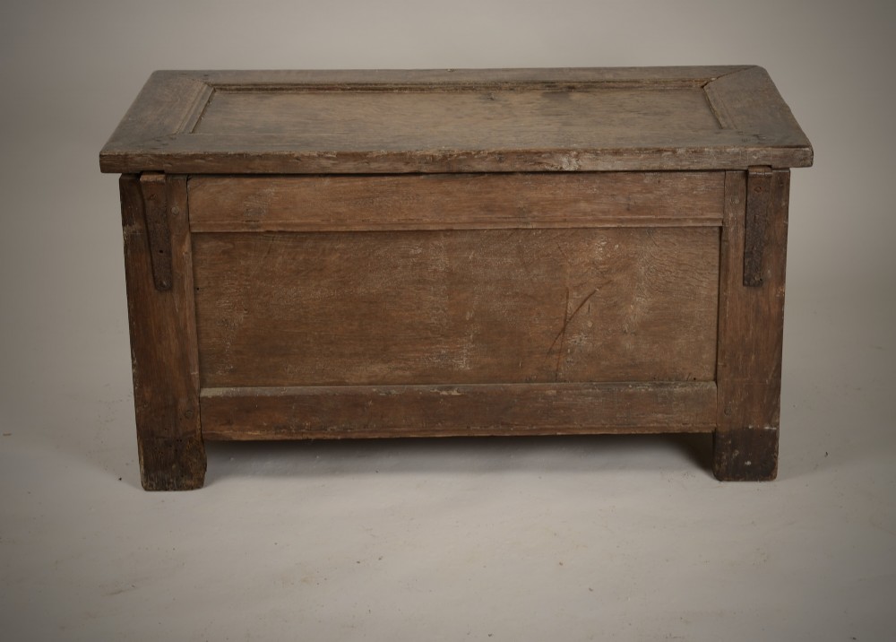 A dark 16th-century oak coffer featuring a hinged panelled lid, framed front panels, a central wrought-iron lock plate, and sturdy stile feet. View VI