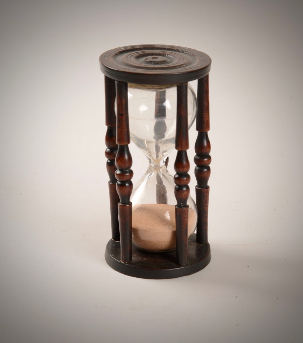 An early nineteenth-century nautical hourglass featuring a hand-blown glass vessel filled with sand, enclosed within a dark turned-wood frame.