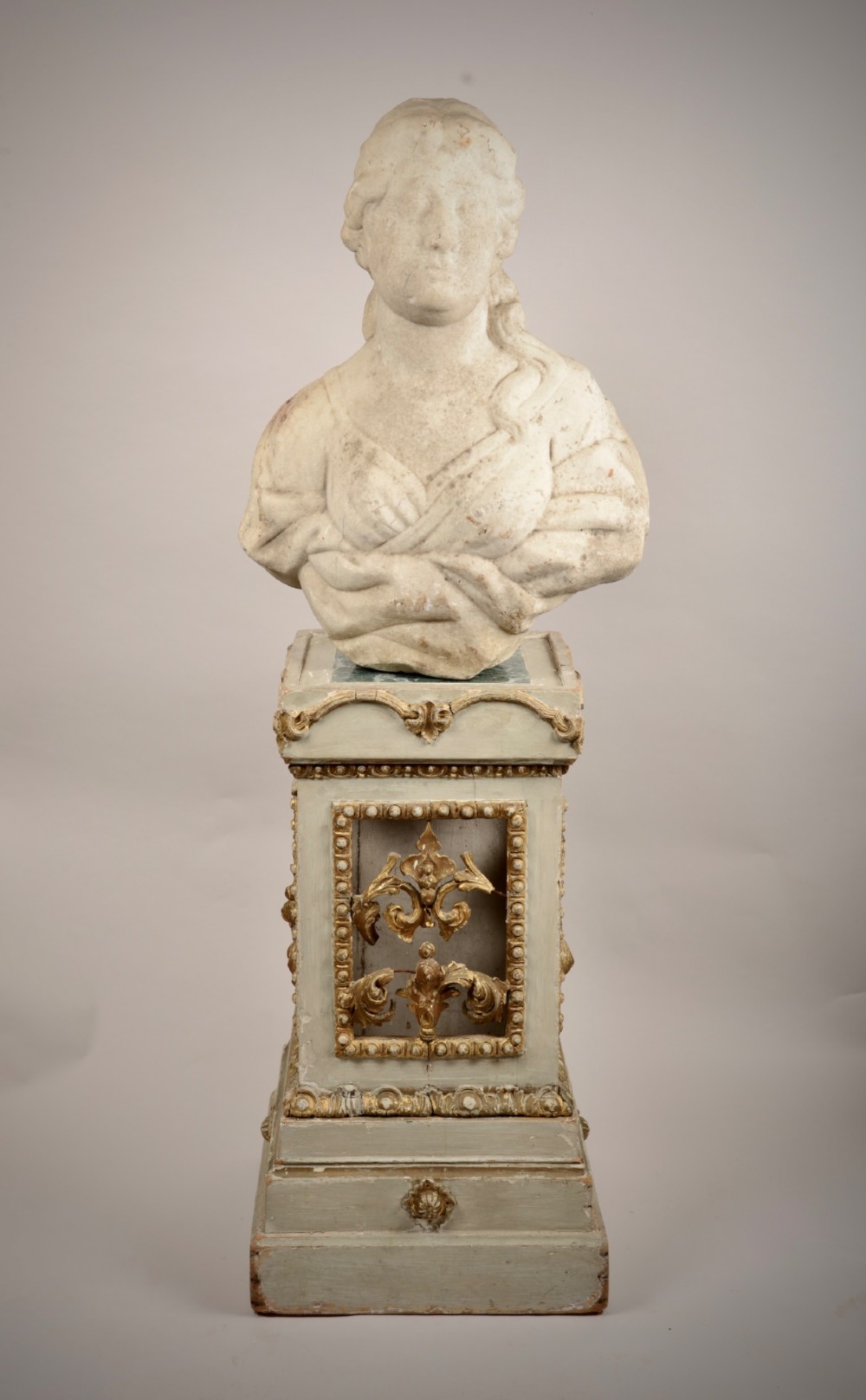 A carved off-white marble bust of a woman with classical draped clothing resting on a painted and gilded wooden pedestal.