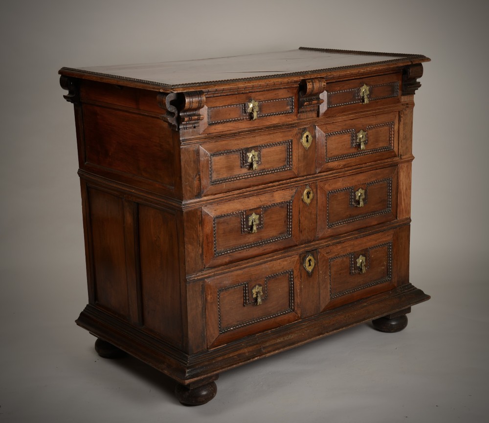 An antique warm brown walnut chest of drawers featuring geometric moulded drawer fronts, brass drop handles, and turned bun feet. View II