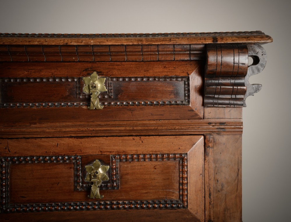 An antique warm brown walnut chest of drawers featuring geometric moulded drawer fronts, brass drop handles, and turned bun feet. View III