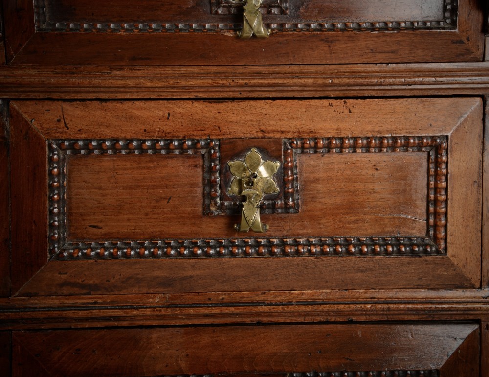 An antique warm brown walnut chest of drawers featuring geometric moulded drawer fronts, brass drop handles, and turned bun feet. View IV