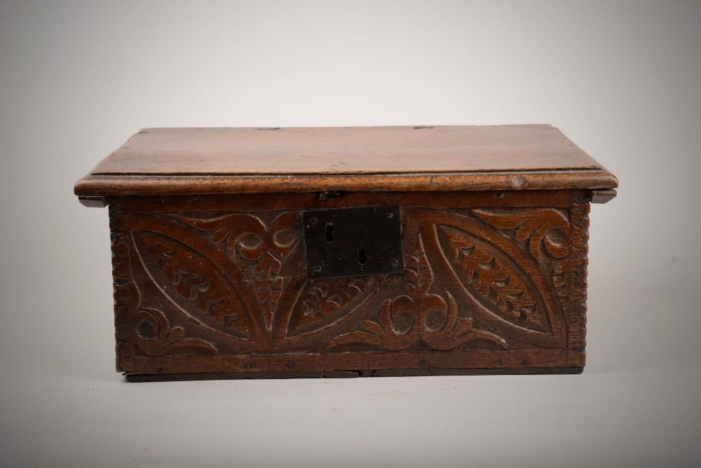 A seventeenth-century dark oak table box with relief-carved leaf and botanical scrollwork on the front panel and a central iron escutcheon plate.