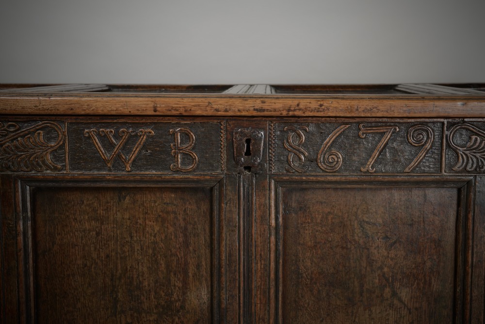 A seventeenth-century dark oak mule chest featuring four carved front panels, three lower drawers, and a carved top frieze with the initials WB and date 1679. View II