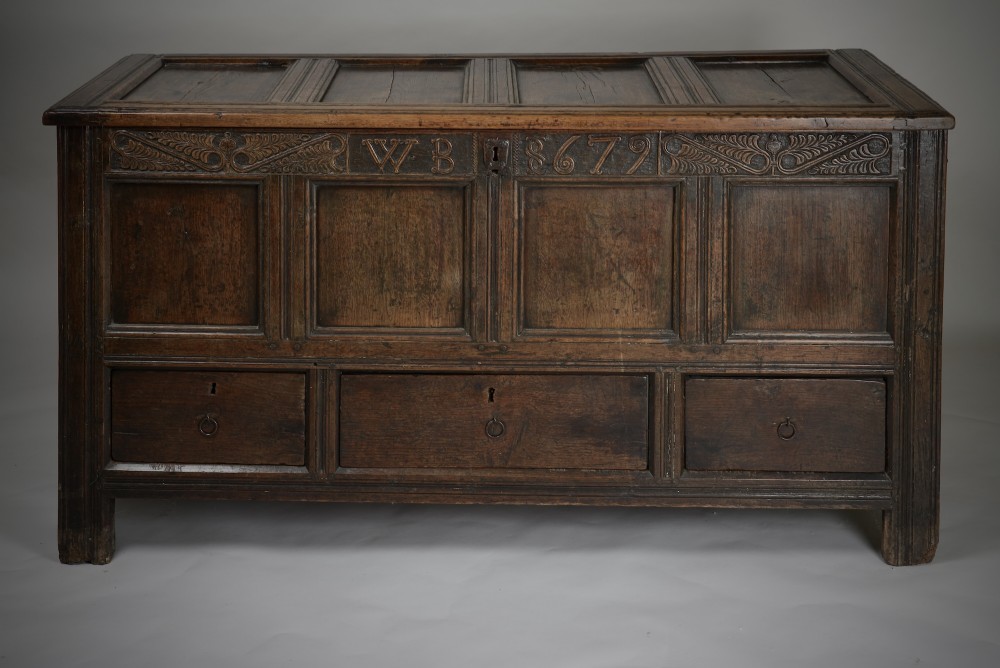 A seventeenth-century dark oak mule chest featuring four carved front panels, three lower drawers, and a carved top frieze with the initials WB and date 1679. View VI
