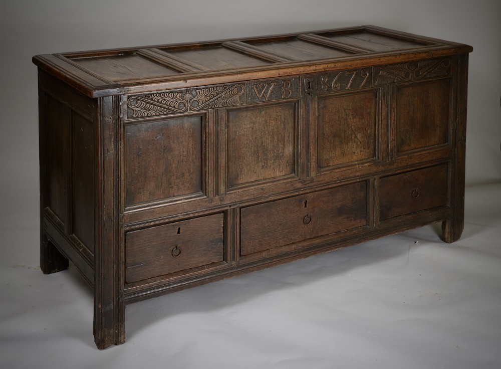 A seventeenth-century dark oak mule chest featuring four carved front panels, three lower drawers, and a carved top frieze with the initials WB and date 1679. View VII