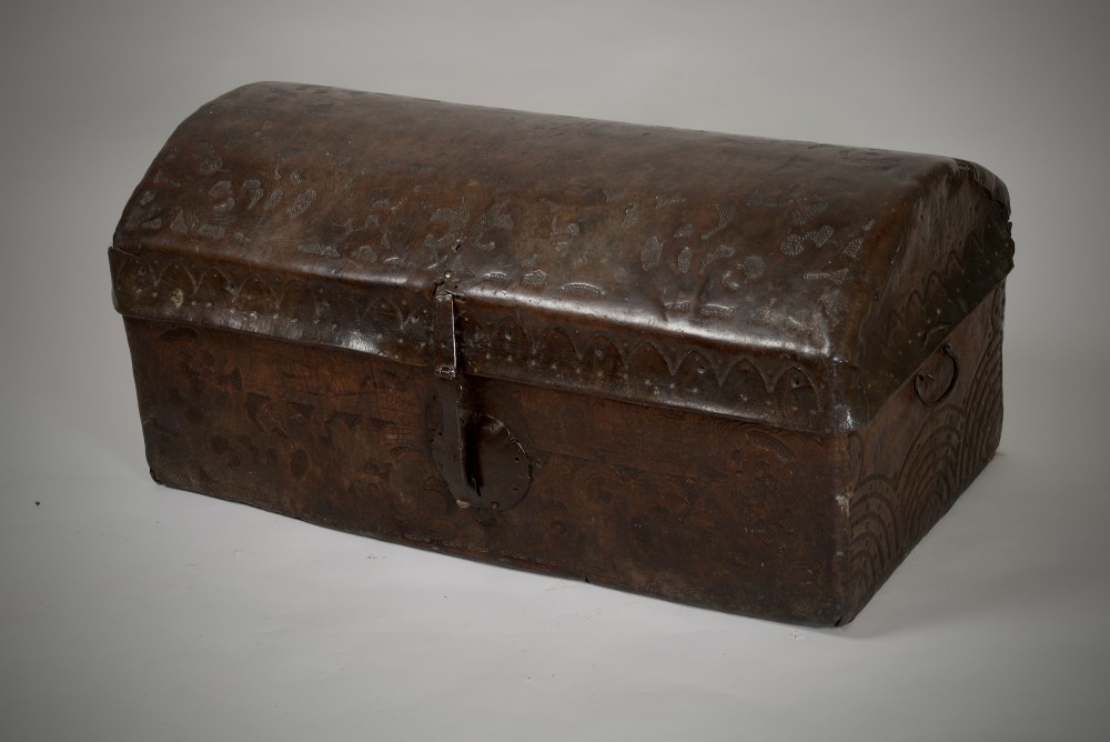 A 17th-century dark brown tooled leather coffer featuring a curved domed lid and central wrought iron lock plate.