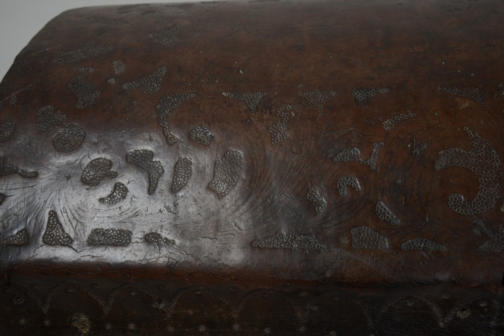 A 17th-century dark brown tooled leather coffer featuring a curved domed lid and central wrought iron lock plate. View V