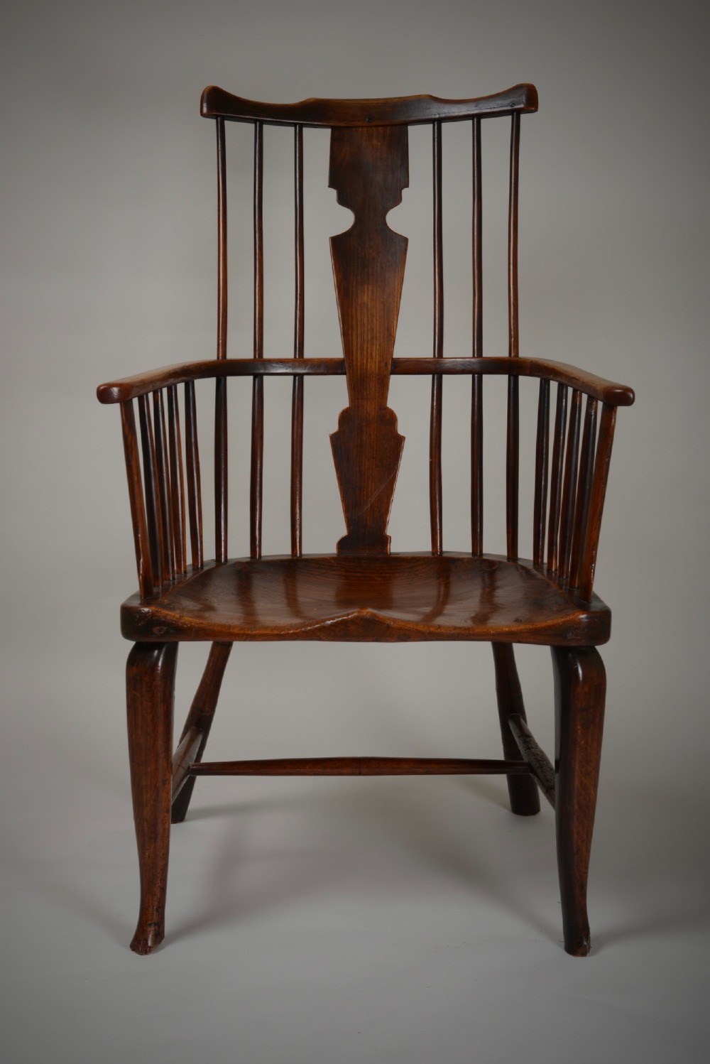 A dark brown antique wooden comb-back Windsor armchair featuring a shaped central splat, slim spindles, a contoured saddle seat, and turned legs. View II