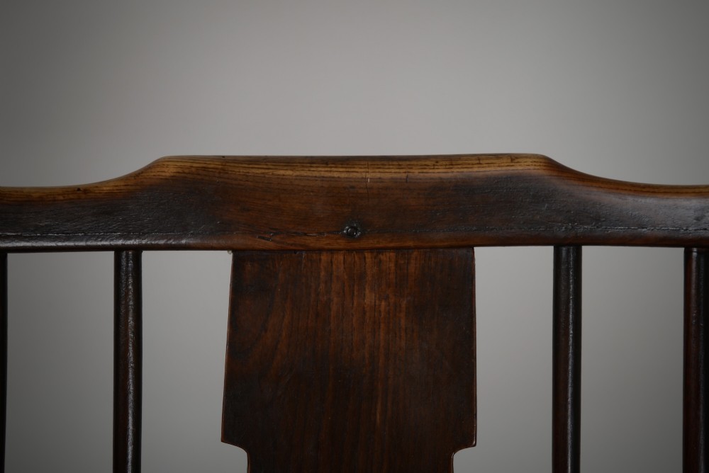 A dark brown antique wooden comb-back Windsor armchair featuring a shaped central splat, slim spindles, a contoured saddle seat, and turned legs. View III