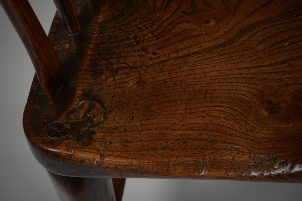 A dark brown antique wooden comb-back Windsor armchair featuring a shaped central splat, slim spindles, a contoured saddle seat, and turned legs. View IV