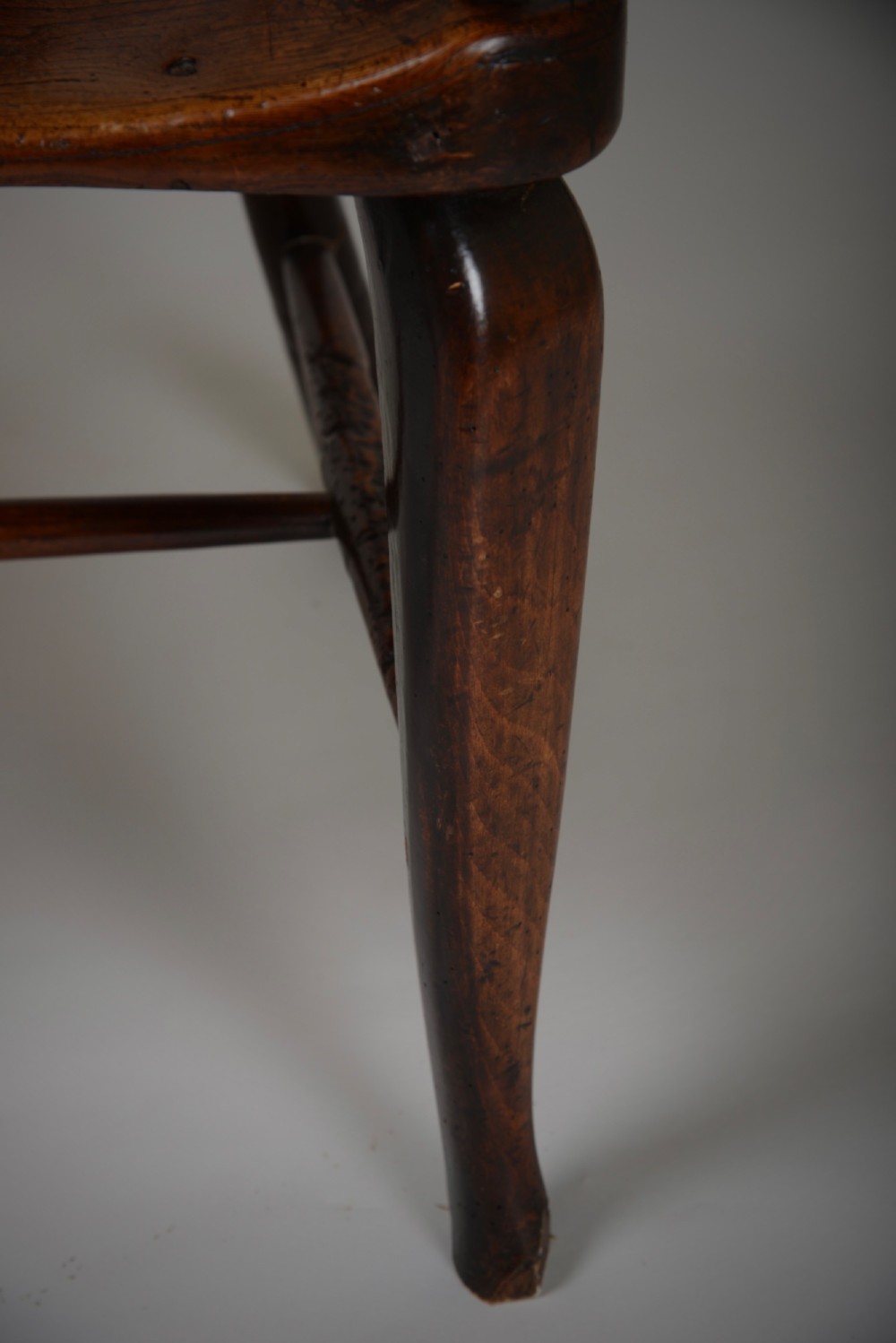 A dark brown antique wooden comb-back Windsor armchair featuring a shaped central splat, slim spindles, a contoured saddle seat, and turned legs. View V