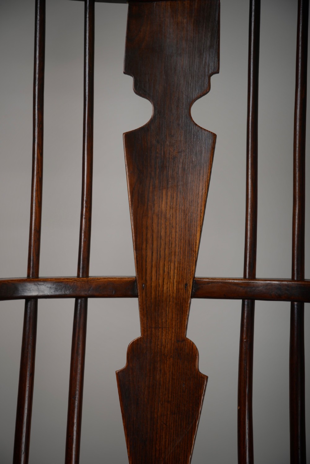 A dark brown antique wooden comb-back Windsor armchair featuring a shaped central splat, slim spindles, a contoured saddle seat, and turned legs. View VI