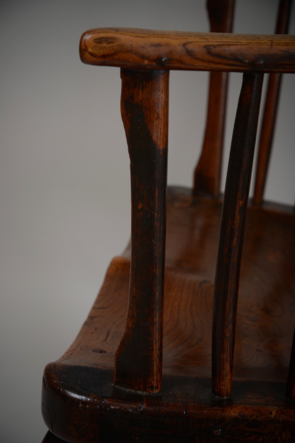 A dark brown antique wooden comb-back Windsor armchair featuring a shaped central splat, slim spindles, a contoured saddle seat, and turned legs. View VII