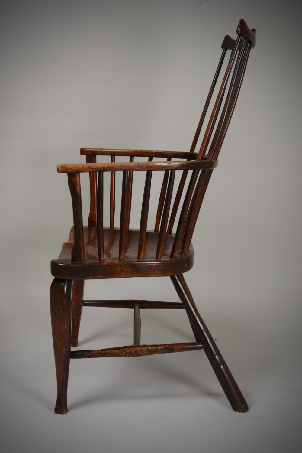 A dark brown antique wooden comb-back Windsor armchair featuring a shaped central splat, slim spindles, a contoured saddle seat, and turned legs. View IX