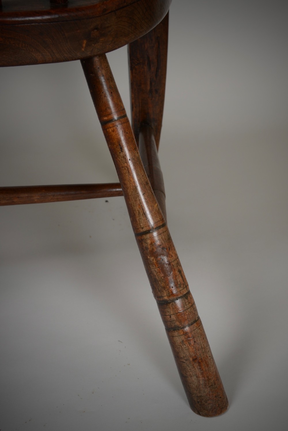 A dark brown antique wooden comb-back Windsor armchair featuring a shaped central splat, slim spindles, a contoured saddle seat, and turned legs. View XI