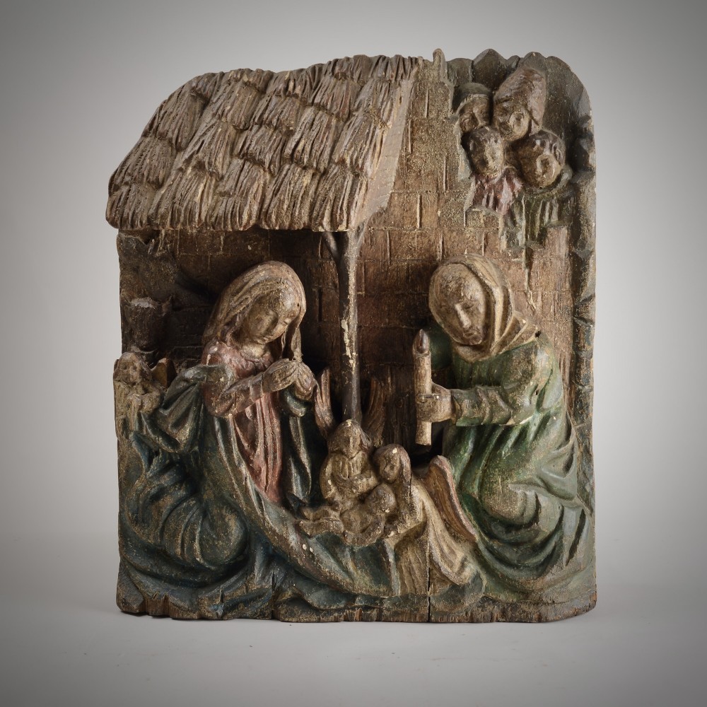 A late medieval carved wooden relief depicting the nativity with Mary, Joseph, and the Christ child under a thatched roof structure with traces of original polychrome paint.