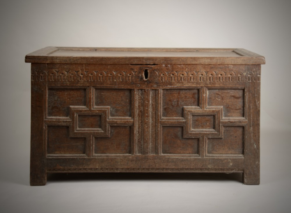 A late Elizabethan dark oak coffer featuring geometric carved front panels, an arcaded frieze, and a central keyhole.