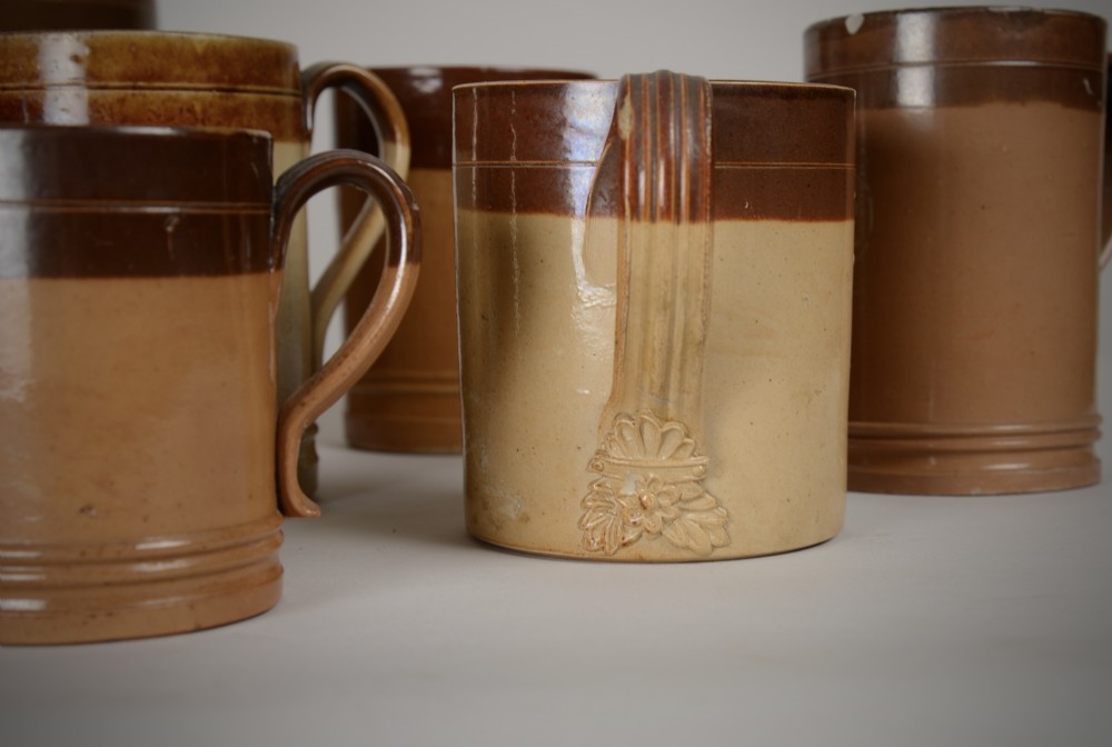 A collection of antique two-tone salt-glazed stoneware tavern mugs and tankards in shades of brown and buff tan. View II