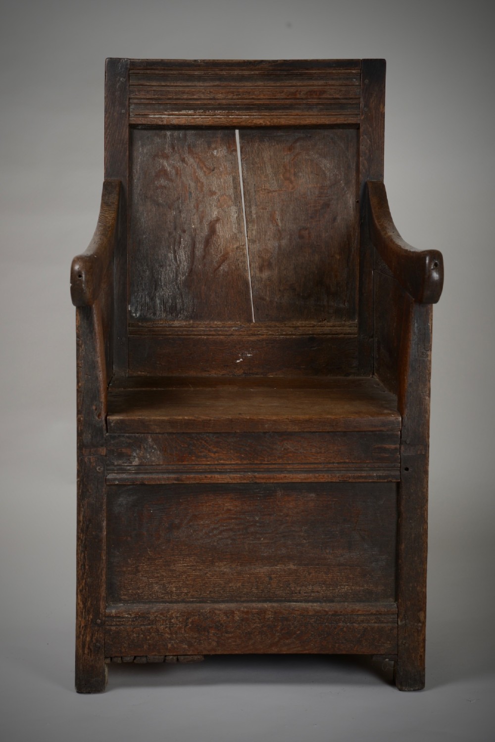 A dark oak late Elizabethan box chair featuring a high panelled back, curved armrests, and an enclosed wooden base. View II