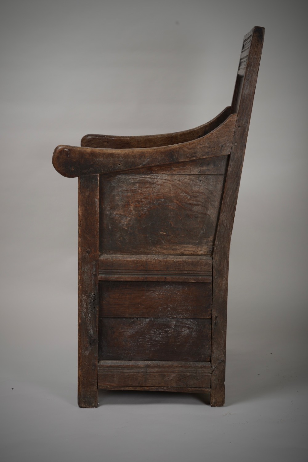 A dark oak late Elizabethan box chair featuring a high panelled back, curved armrests, and an enclosed wooden base. View V