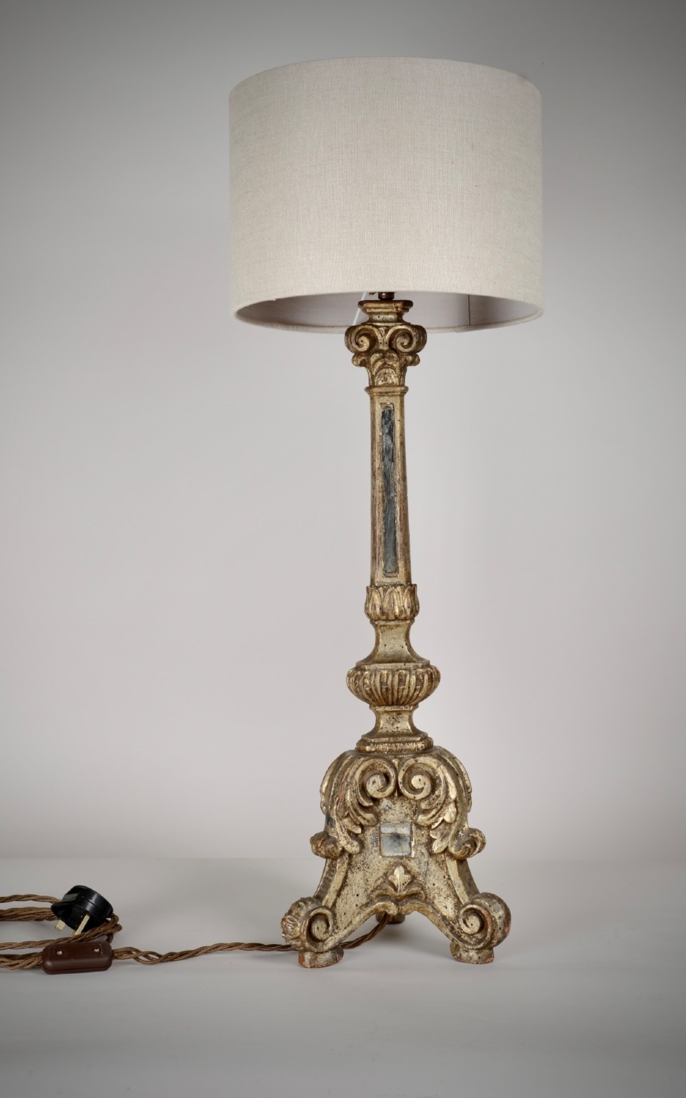 A tall table lamp featuring an 18th-century Italian carved giltwood candlestick base paired with a neutral linen drum shade.