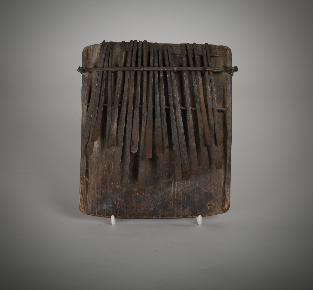 A hand-carved dark wood thumb piano fitted with numerous hand-forged iron tines held down by a wire bridge.