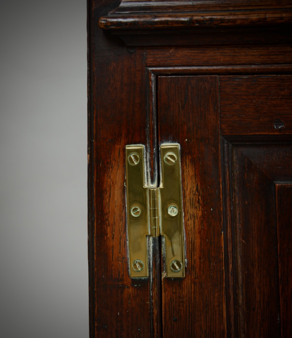 An 18th-century dark oak dresser base featuring three drawers over two cupboard doors flanking a central arched fielded panel with brass hardware. View IV