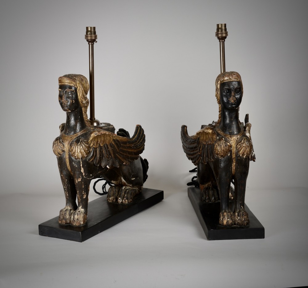 A pair of 18th-century ebonised and parcel-gilt carved wooden sphinx sculptures mounted on rectangular plinths and converted into table lamps with black shades. View II
