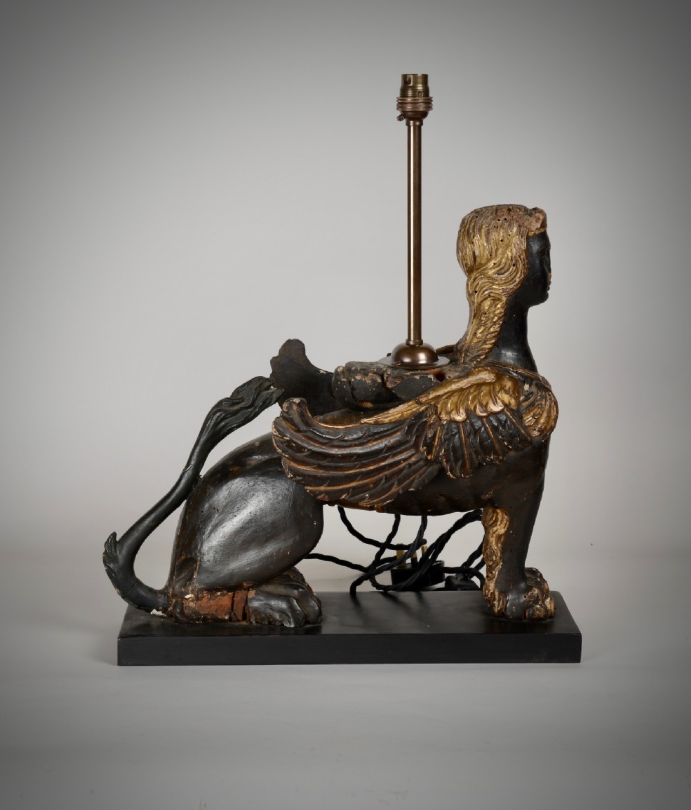 A pair of 18th-century ebonised and parcel-gilt carved wooden sphinx sculptures mounted on rectangular plinths and converted into table lamps with black shades. View IV