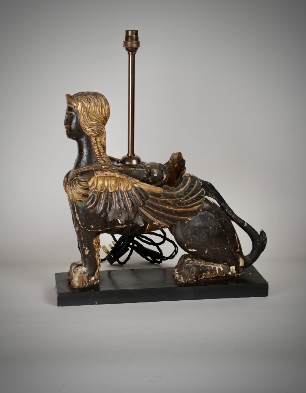 A pair of 18th-century ebonised and parcel-gilt carved wooden sphinx sculptures mounted on rectangular plinths and converted into table lamps with black shades. View V