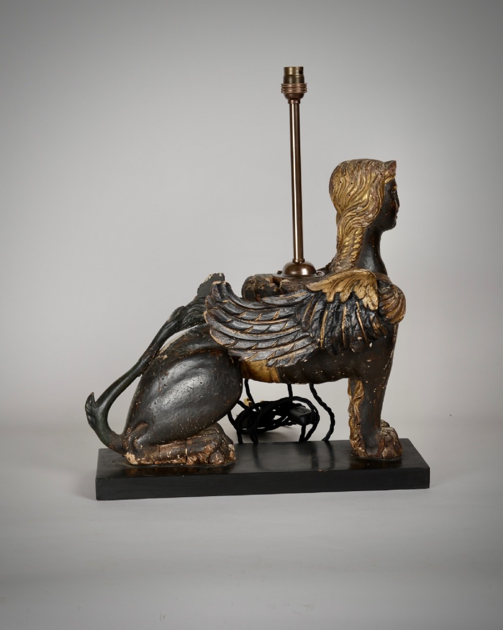 A pair of 18th-century ebonised and parcel-gilt carved wooden sphinx sculptures mounted on rectangular plinths and converted into table lamps with black shades. View VI