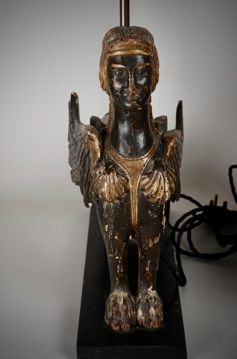 A pair of 18th-century ebonised and parcel-gilt carved wooden sphinx sculptures mounted on rectangular plinths and converted into table lamps with black shades. View IX