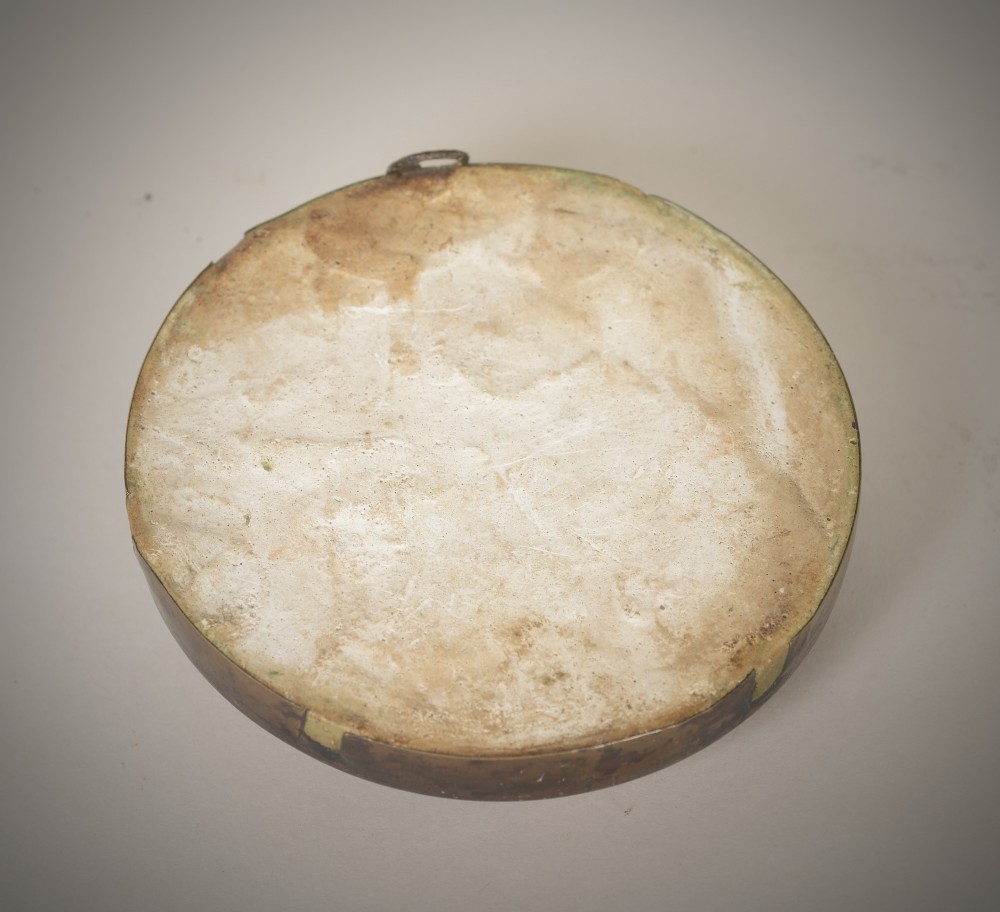 A round beige plaster relief capturing figures carved in high relief, secured inside a circular metal frame with a hanging loop at the top. View III