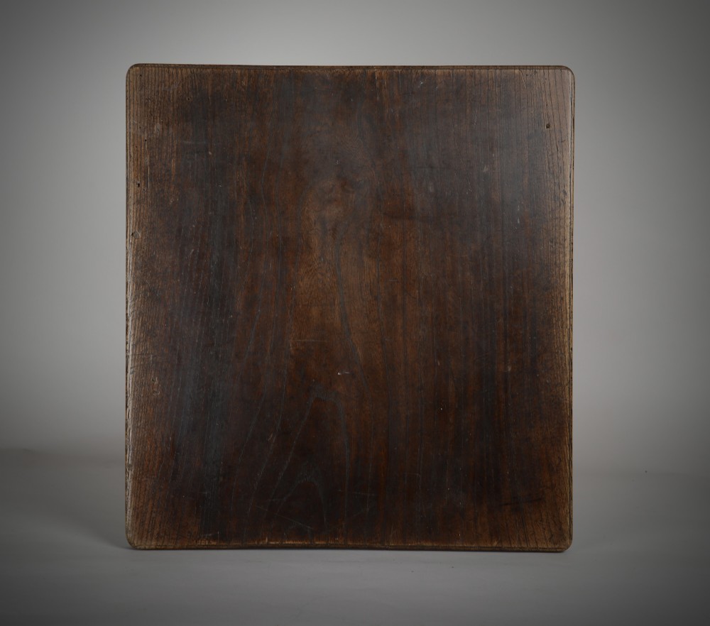 A square dark oak treen serving board with rounded corners, showing natural grain and aged surface patina.