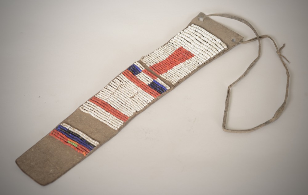 An antique Native American leather hide strip featuring geometric glass seed beadwork in white, red, blue, and green with hide ties attached.