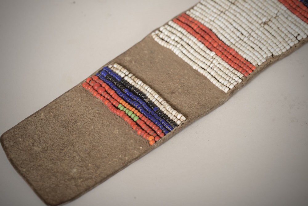 An antique Native American leather hide strip featuring geometric glass seed beadwork in white, red, blue, and green with hide ties attached. View II