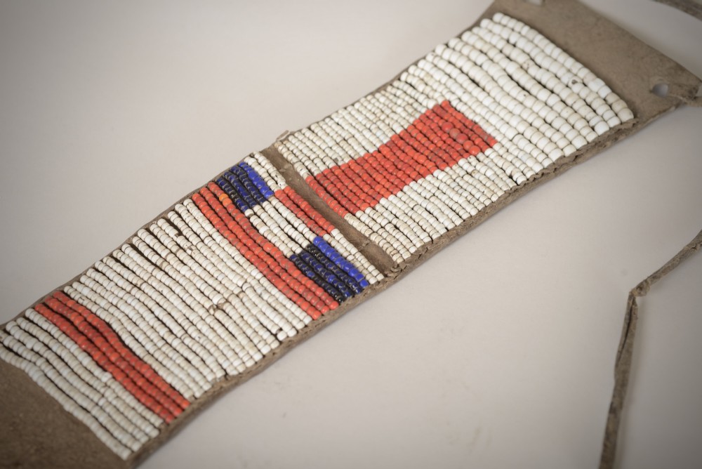 An antique Native American leather hide strip featuring geometric glass seed beadwork in white, red, blue, and green with hide ties attached. View III