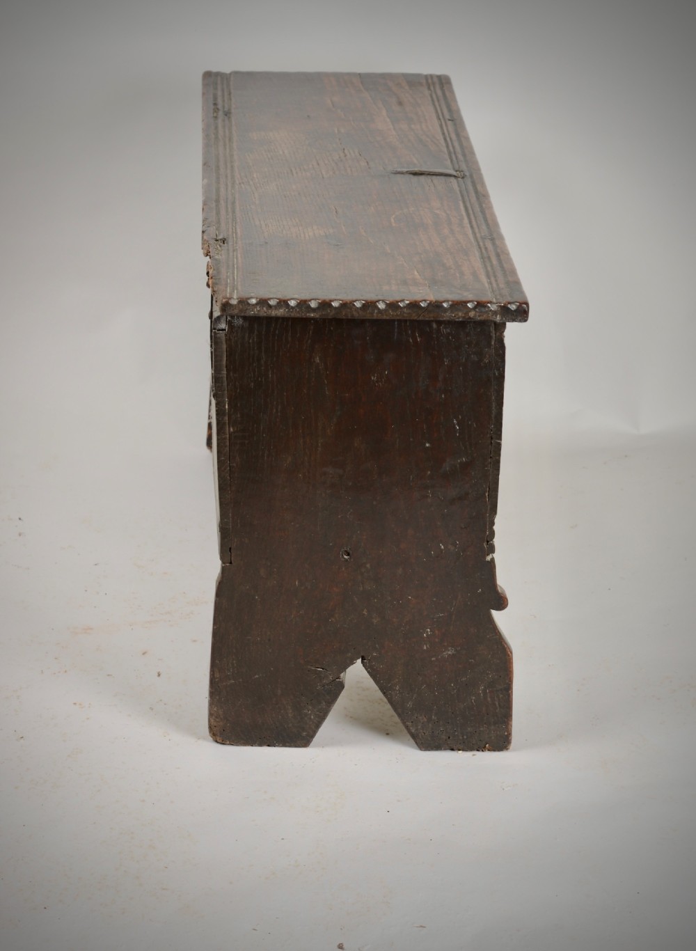 A small antique dark oak six-plank coffer featuring an incised moulded top lid, hand-forged iron lockplate, and V-cut bootjack slab ends. View VIII