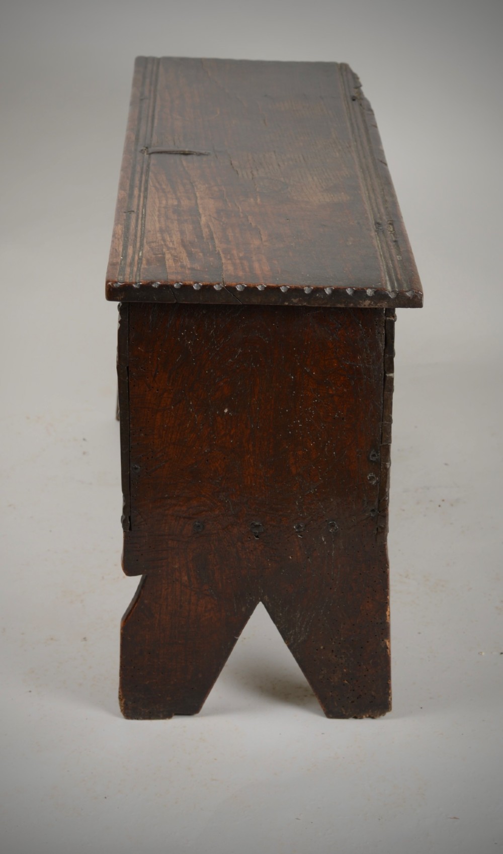 A small antique dark oak six-plank coffer featuring an incised moulded top lid, hand-forged iron lockplate, and V-cut bootjack slab ends. View IX