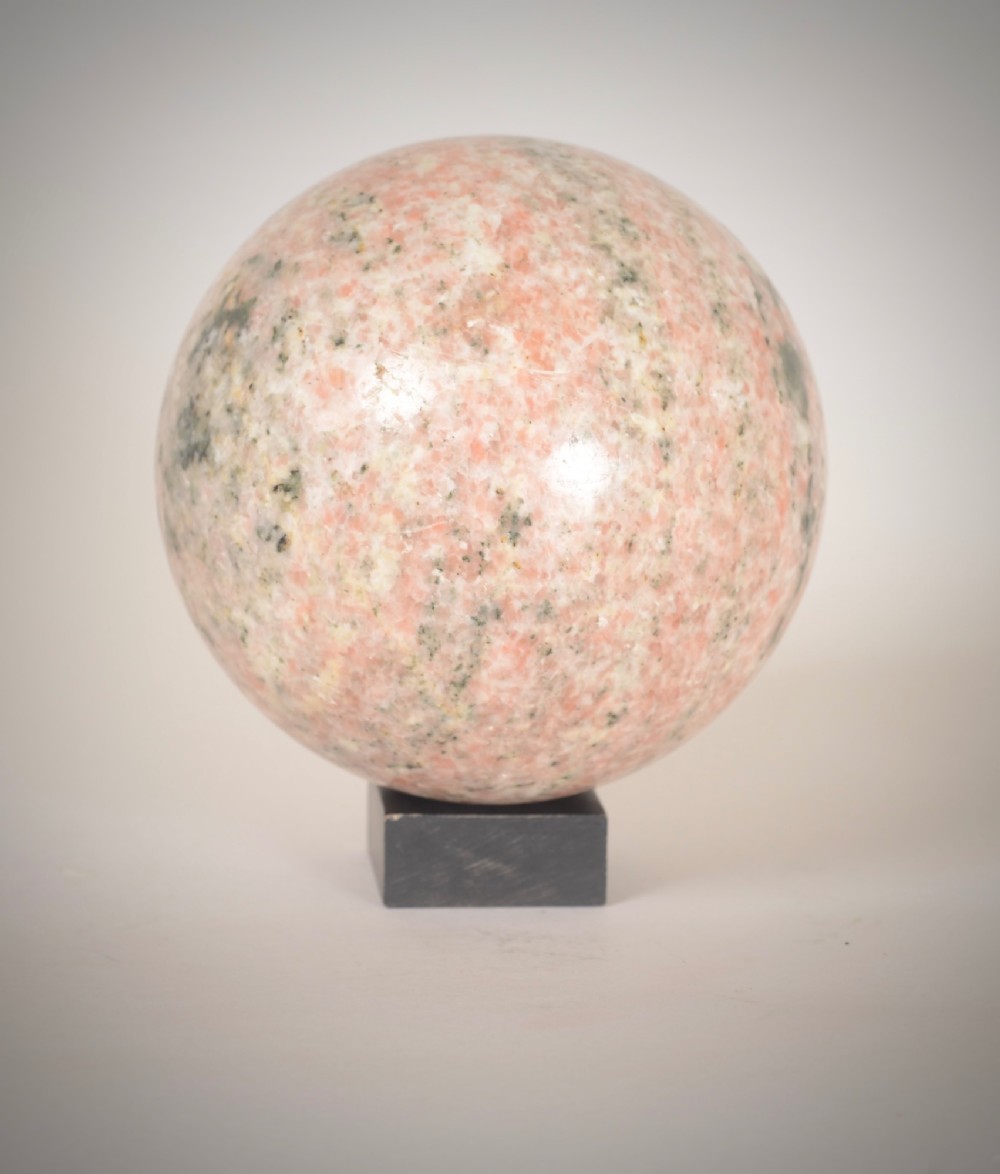 A polished pink granite sphere with grey speckled inclusions rests on a small dark square base.