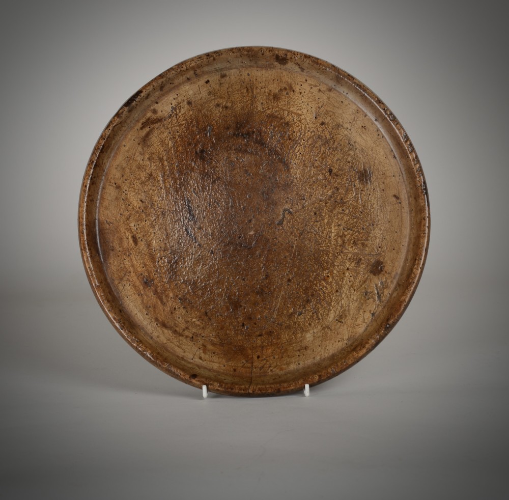 A shallow circular hand-turned wooden treen platter featuring a raised rim and rich aged timber patina. View II