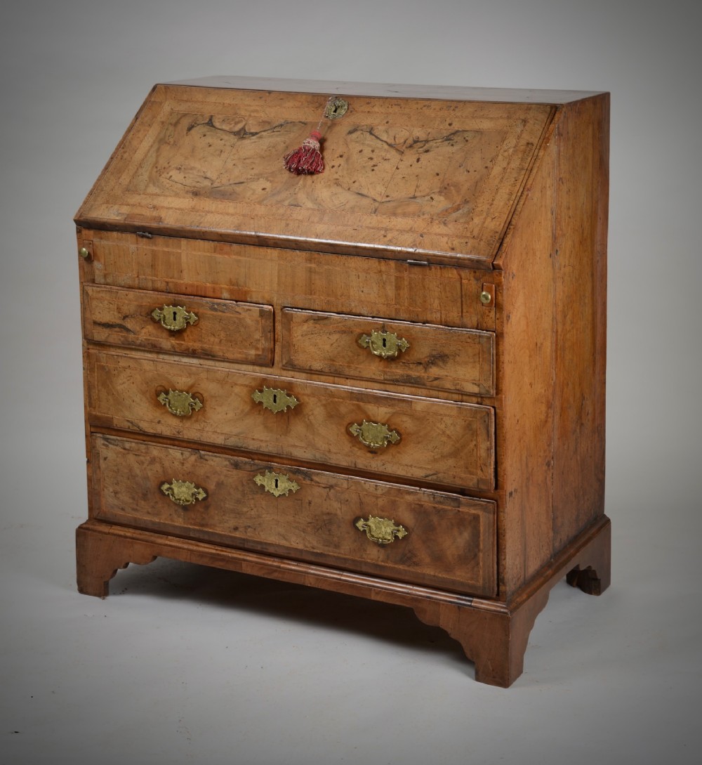 An 18th-century George II burr walnut bureau featuring a sloped fall-front flap above four graduated drawers with brass handles and bracket feet. View X